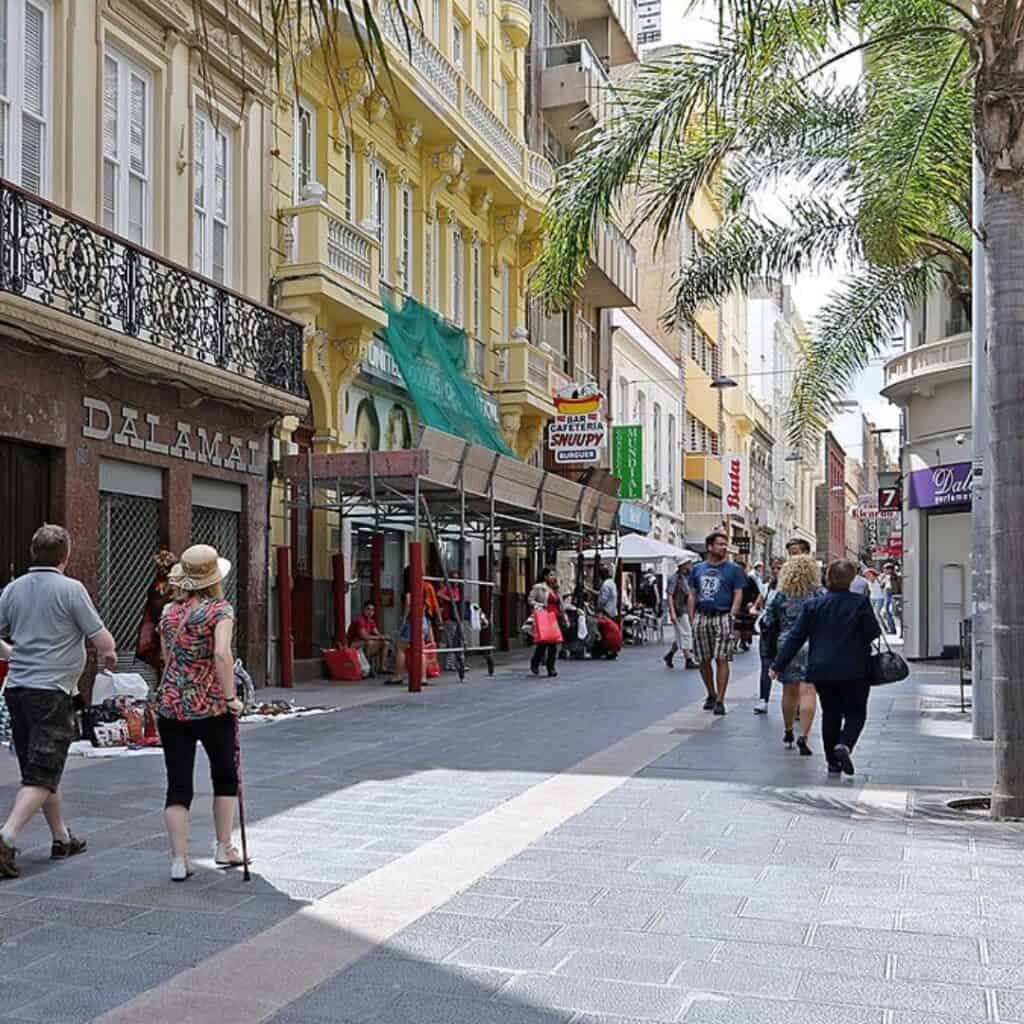 people walking down a Calle del Castillo in a city with shops and palm trees