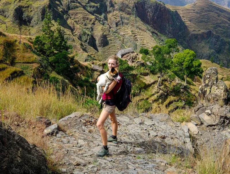 a woman carrying a dog hiking in santo antao with the views of the mountain