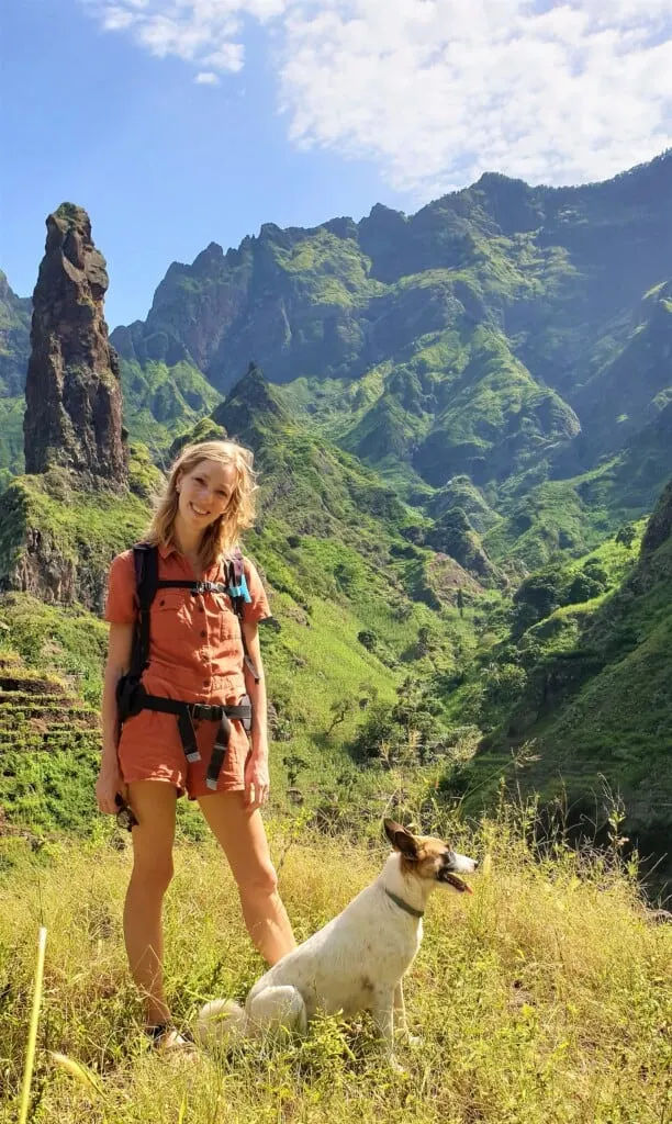 a woman and a dog posing with a view of the mountains on a bright sunny day