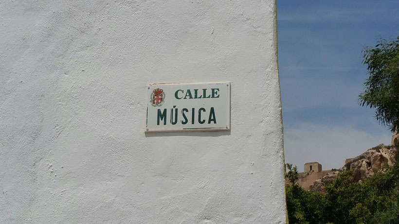 a sign on a white wall with a sign of Calle Musica, almeria street