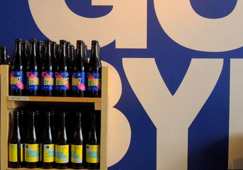 must try traditional brussels food, two shelves of beer next to a wall with large letters in blue and white