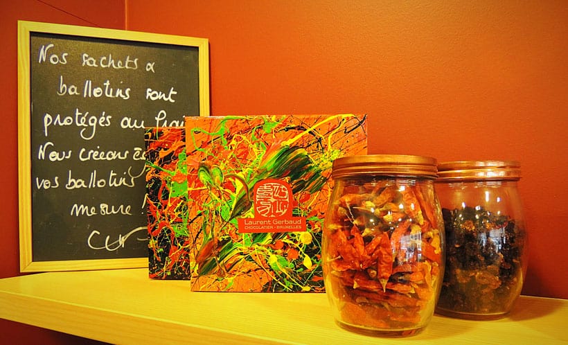 best belgian restaurant brussels has to offer, yellow shelf with jars of chillis and nuts and cards with abstract expressionist art and the restaurant logo in front of a small chalkboard with French written on it