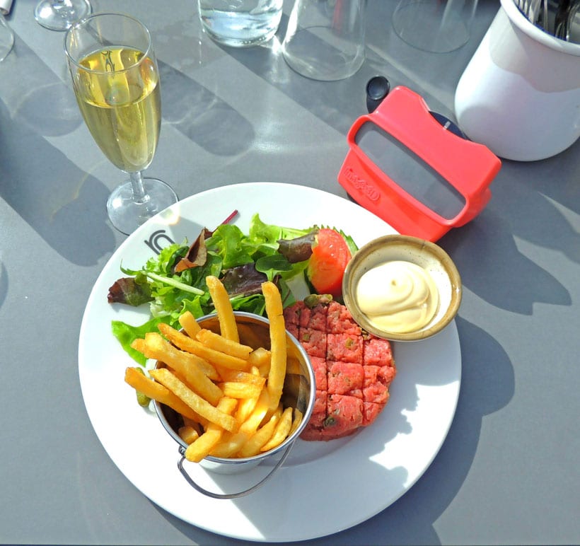 Where to eat Traditional Belgian Food in Brussels, plate of raw steak with french fries, sauce and salad on a table beside a glass of wine and container of cutlery