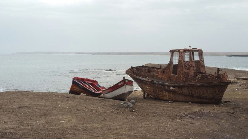 a rusty old boat and a boat torn in half on a  brown sandy beach