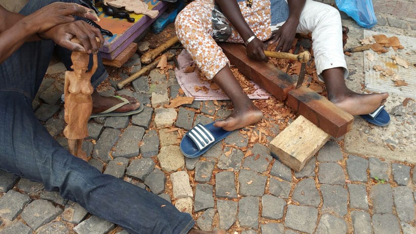 2 cape verdeans sitting on the floor carving a statue from wood