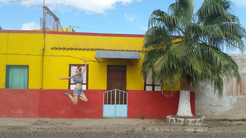 a woman jumping up in front of a red and yellow house with a tree on the front