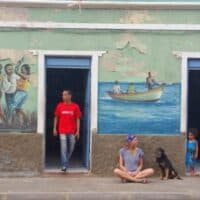 a woman sitting by the streets with dogs, a man by the door, an a child by the door with art painted on the walls