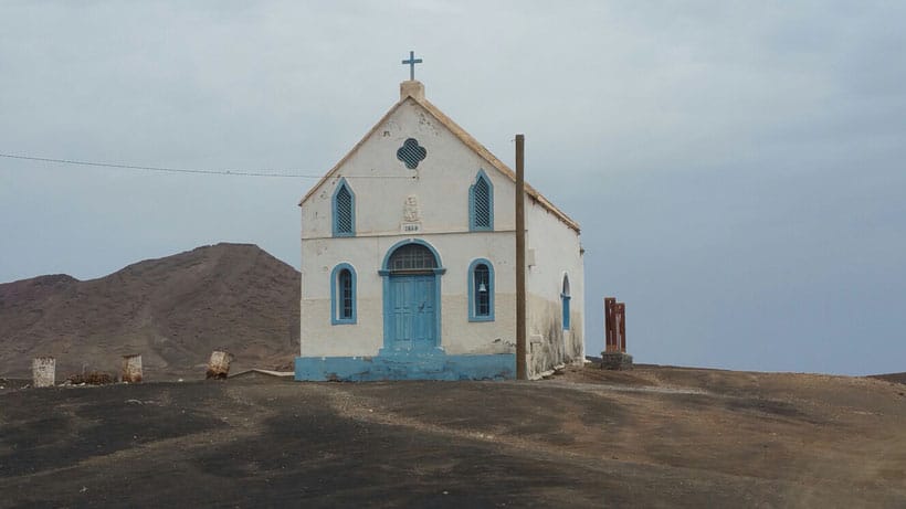 a church in the middle of a beach and a mountain at the back