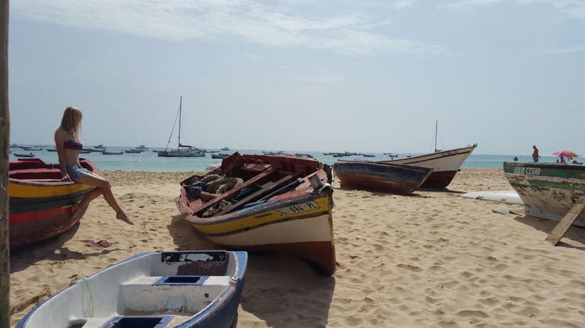 Answer the question of what is there to do in sal cape verde, white sandy beach with colourful boats resting both on the sand and moored nearby out to sea and a blonde woman sitting on the far left boat