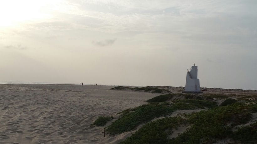 a lighthouse on a beach with people walking on a sunny day