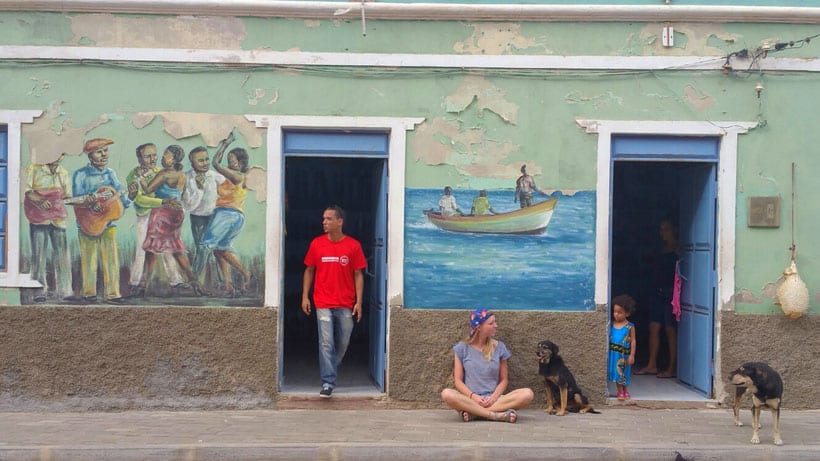 a woman sitting by the streets with dogs, a man by the door, an a child by the door with art painted on the walls