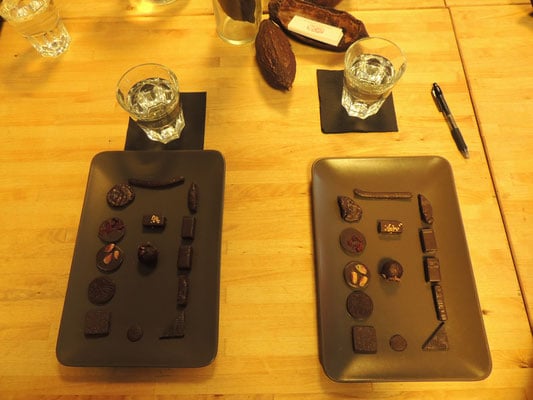 where to get the best belgian food in brussels, two long black plates with rectangle of different chocolates for tasting next to a glass of water