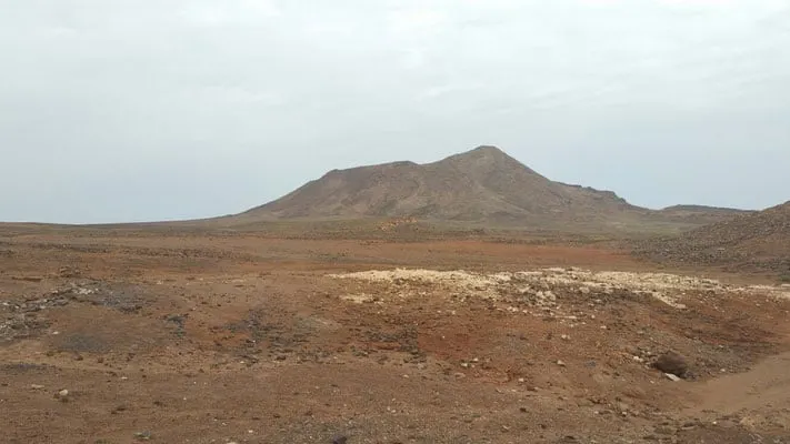 Get lost in the vibrant nightlife in sal, cape verde, wide open plain with a tall mountain in the distance under a grey sky