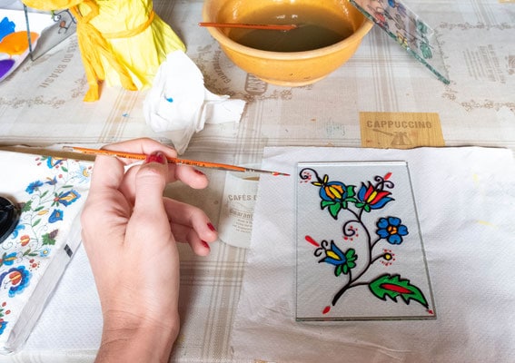 a closeup of a woman's hand with a brush and a painting on a glass