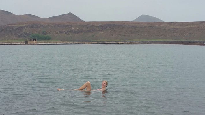 Explore what to do in sal cape verde, person swimming in body of water in front of rolling hillside with peaks of hills in the distance