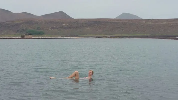 Explore what to do in sal cape verde, person swimming in body of water in front of rolling hillside with peaks of hills in the distance