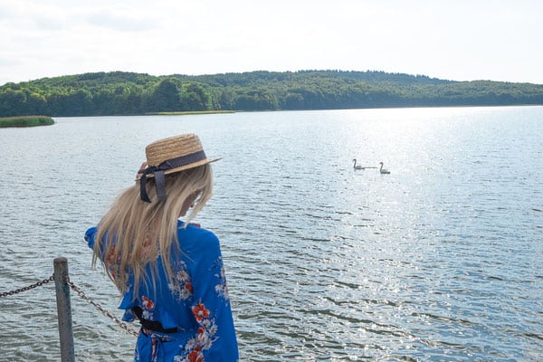 a woman with a hat at the edge of the dock and ducks swimming in kashubian lake district