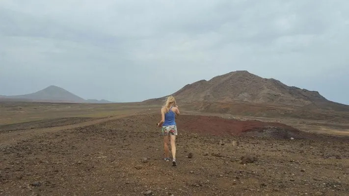 Discover what to do in cape verde sal, person walking off across a wide open plain towards the tall hills and mountains in the distance under a cloudy sky