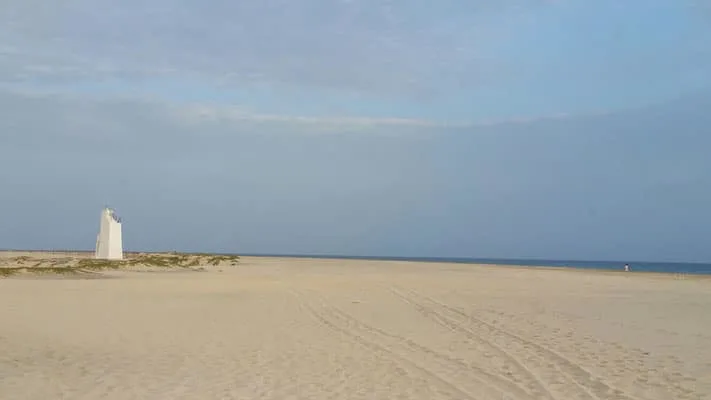 Find out what is there to do in sal cape verde, wide sandy beach with white observation tower structure in the distance under a blue sky with clouds