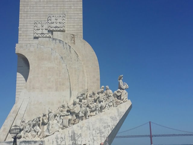 a closeup of a statue with people climbing upwards with a bridge in the background