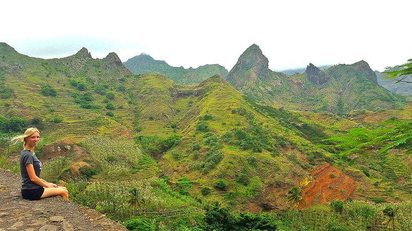 a woman sitting near a cliff with a  view of the mountains, terraces, and the sky