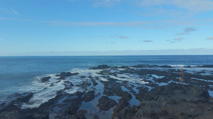 a person on top of rocks looking at swimming pools in sinagoga village by the sea