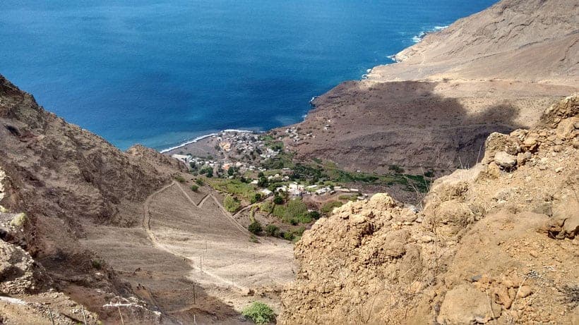 a view of a rocky pathway surrounded by mountains leading to a small town by tarrafal beach