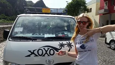 a woman smiling near a car with a sign of "xoxo" on the front