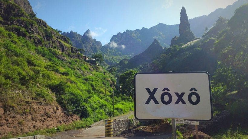 a sign with Xoxo with mountains and a pathway on a bright day