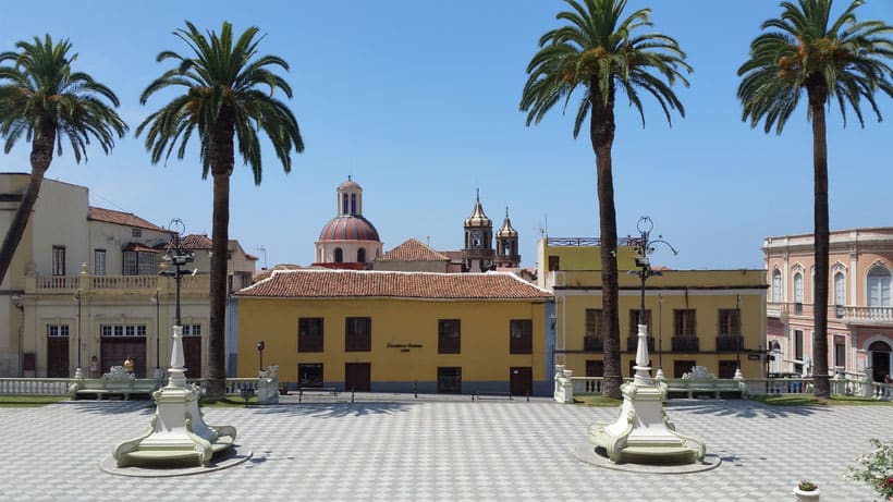 a view of a plaza with  benches, two palm trees orange or yellow buildings 