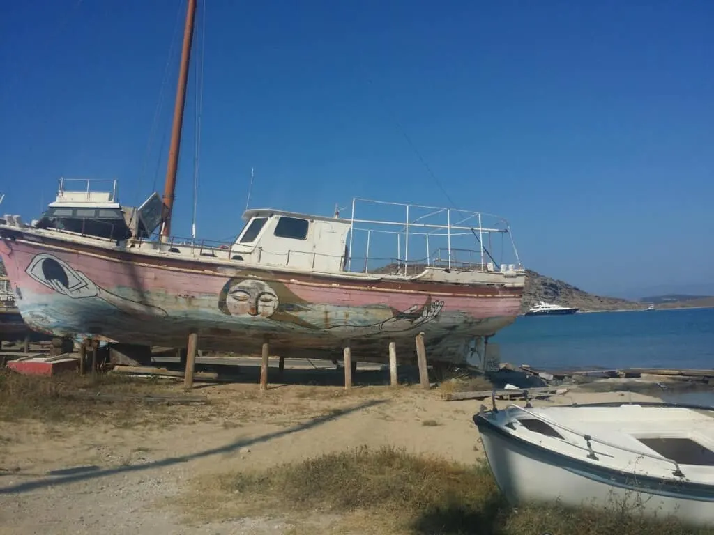 where to go in paros, old boats on the water, one has artwork of woman holding moon and eye on the side