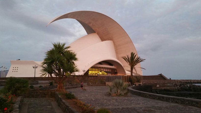 a white crescent shaped roof or building with 2 trees with a stone pathway