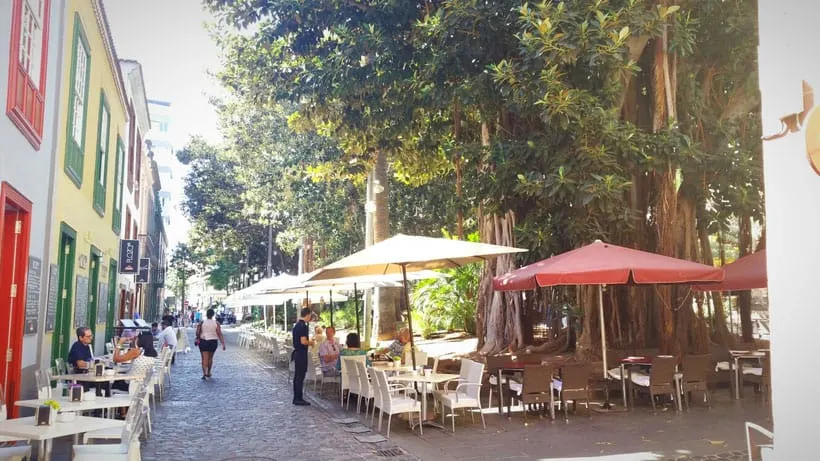 a street lined with cafes, tables and chairs and umbrellas with a few people dining