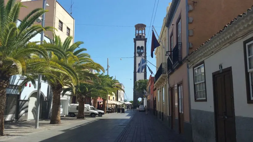 a street lined with palm trees and building leading to a tower