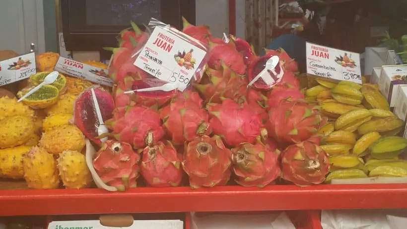 a fruit display with dragon fruit, bananas, and mangoes with prices