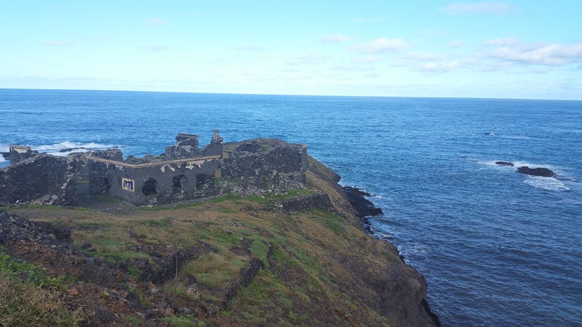 a view of the ruins of a hospital by the cliff with a view of the sea and sky