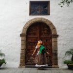 Best places to visit in Tenerife, person wearing traditional costume standing in front of large ornate wooden door in arched stone doorway set in a white walled building with green potted plants to either side