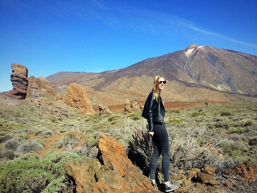 Person standing in front of grassy plain leading up to Mount Teide under a blue sky