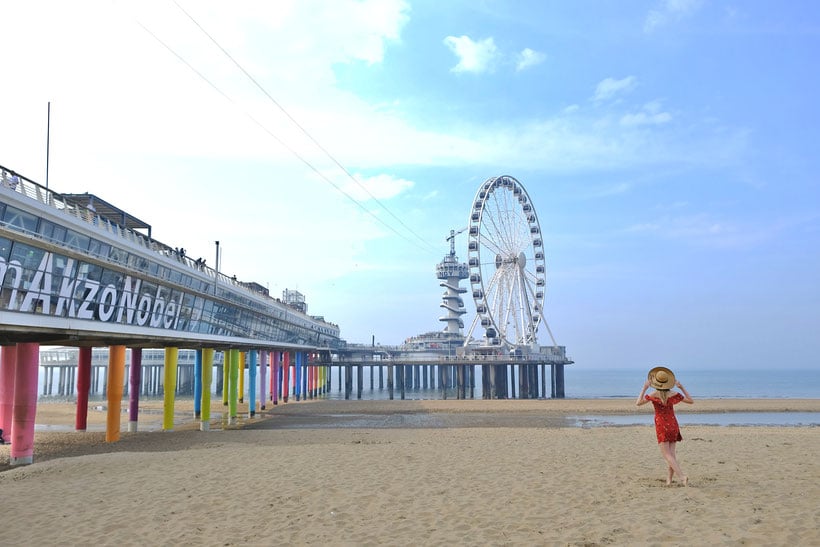 a pier by the beach with a ferris wheel and a woman posing