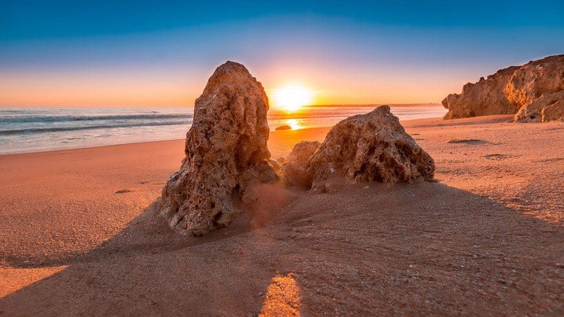 things to do in algarve portugal, rock formation on sandy algarve beach at sunset