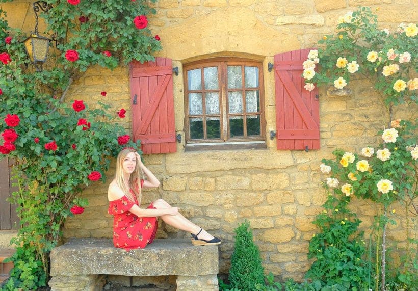 a woman sitting by the stone chair near a red window and a brick wall