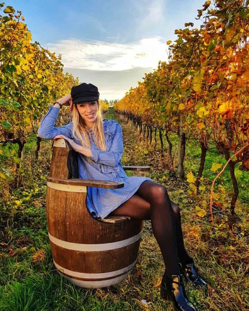 a woman sitting and posing in front of a camera in a vineyard