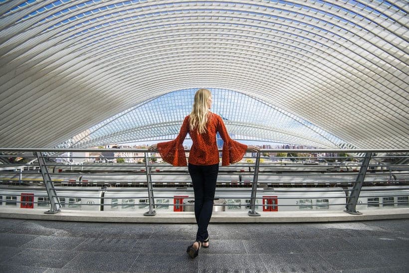 a woman standing in the train station looking out at liege