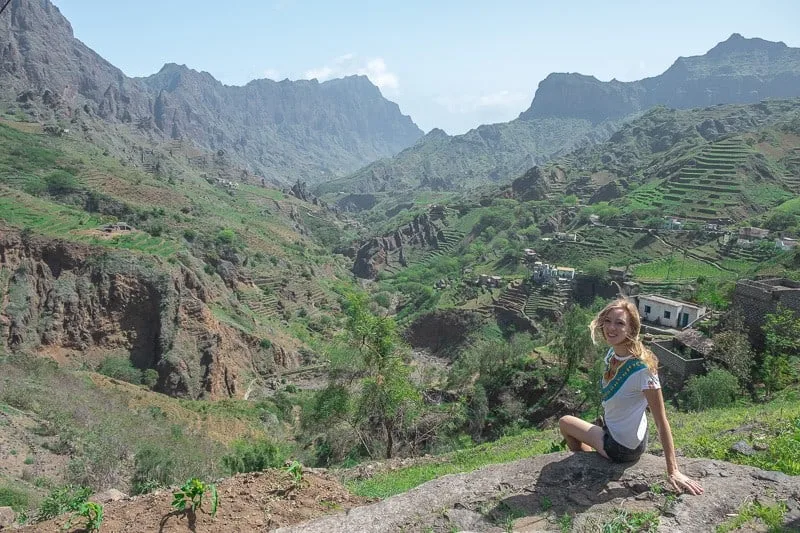 a view of a woman smiling and looking at with a view of the ribeira grande mountains and a small town