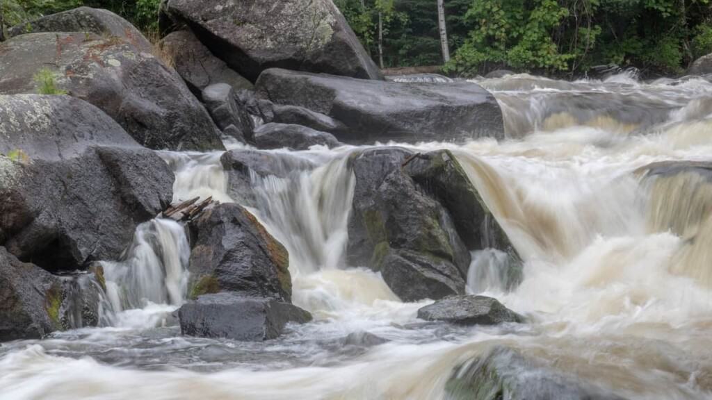 a picture of a short waterfall filled with rocks and brownish water