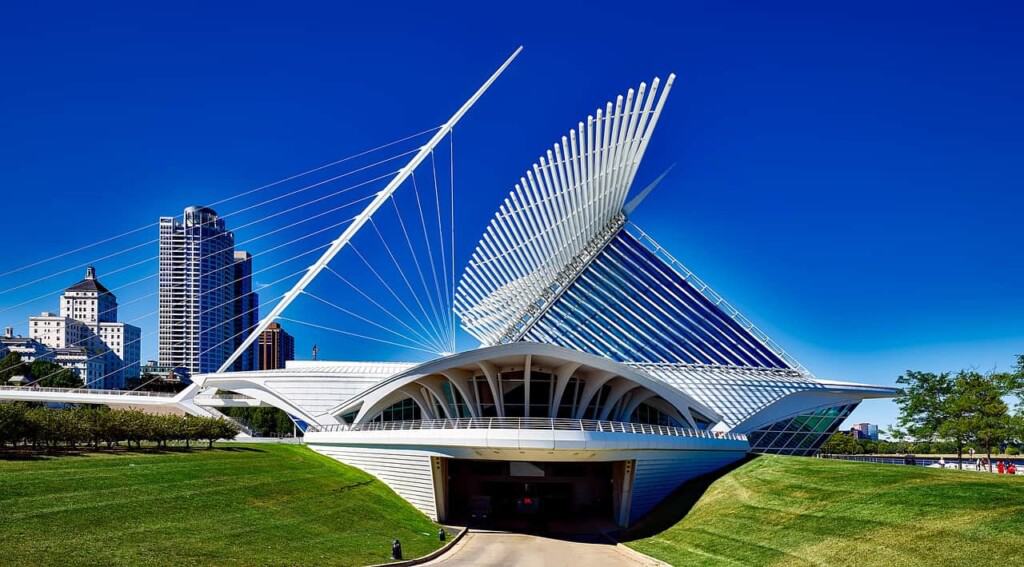 a white state of the art building in milwaukee with a walkway surrounded by grass and buildings at the back