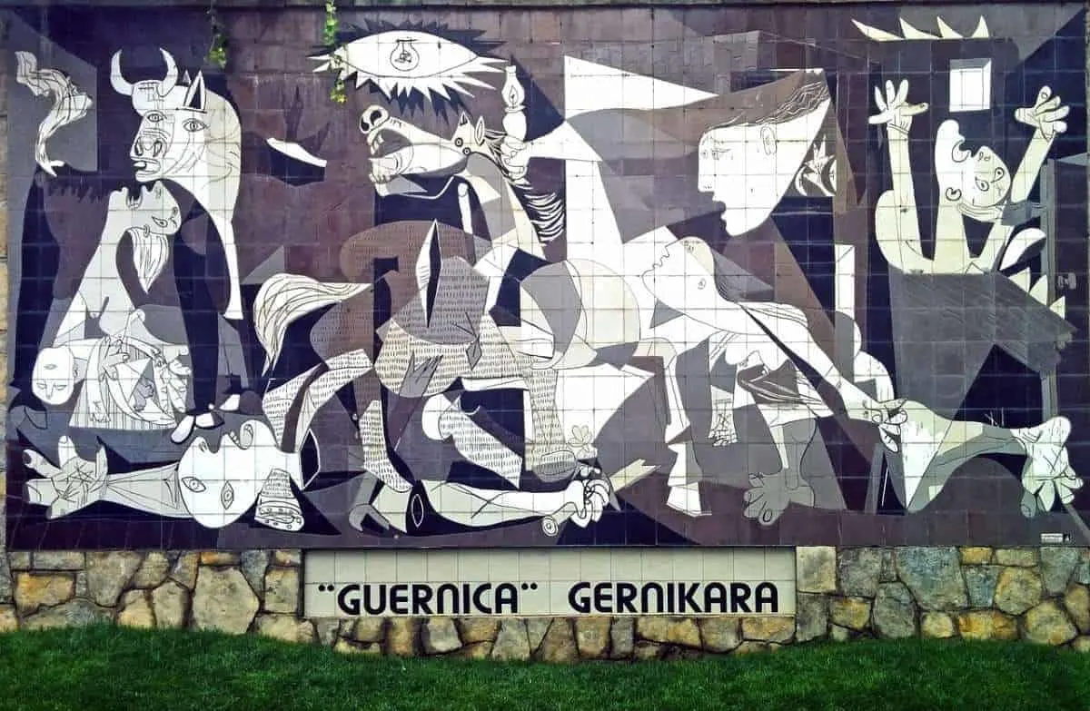 The famous work Guernica by Picasso is featured at the Reina Sofia Museum. This image shows the painting, an abstract depiction of faces and bodies in a war in shades of grey, black, and white. 