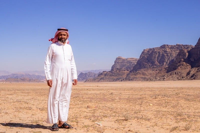 Discover what to wear to Wadi Rum this summer, Saleem, the manager of Wadi Rum Quiet Village standing in the desert with large rocky mountains behind