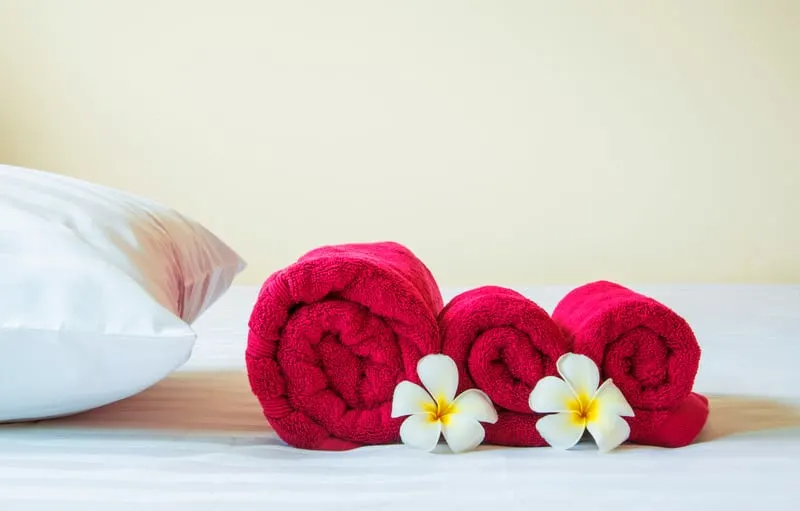 looking for romantic things to do in Appleton, close up shot of three red towels neatly folded and placed on top of a white bed next to a soft white pillow with two delicate and decorative white and yellow flowers