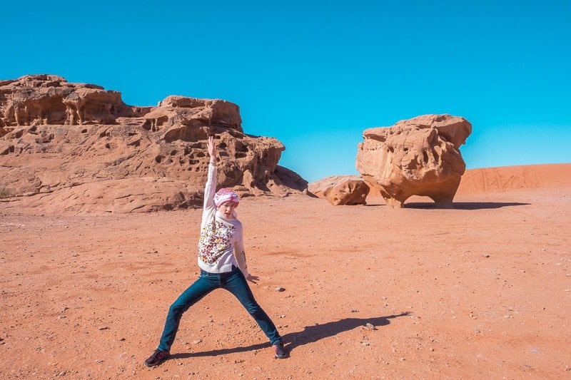 Find out what to do at Wadi Rum, person making powerful shapes in the desert in front of large rocks under a clear azure blue sky